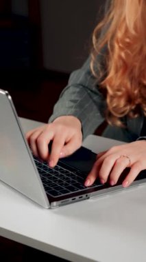 Kızıl saçlı genç bir kadın dizüstü bilgisayarda çalışıyor. Bir kız öğrenci dizüstü bilgisayarda çalışıyor. Uzaktan kumanda konsepti. Bir ofis çalışanının portresi. Eller dizüstü bilgisayarda. Dikey video .4k