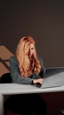 Kızıl saçlı genç bir kadın dizüstü bilgisayarda çalışıyor. Bir kız öğrenci dizüstü bilgisayarda çalışıyor. Uzaktan kumanda konsepti. Bir ofis çalışanının portresi. Eller dizüstü bilgisayarda. Dikey video .4k