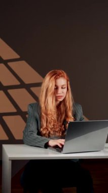 Bir kadın ofisteki başarısına sevinir. Genç bir kadın dizüstü bilgisayarın başında otururken güler ve sevinir. Mutlu bir serbest çalışanın portresi. Çevrimiçi iş kavramı. Dikey video