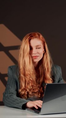 Bir kadın ofisteki başarısına sevinir. Genç bir kadın dizüstü bilgisayarın başında otururken güler ve sevinir. Mutlu bir serbest çalışanın portresi. Çevrimiçi iş kavramı. Dikey video