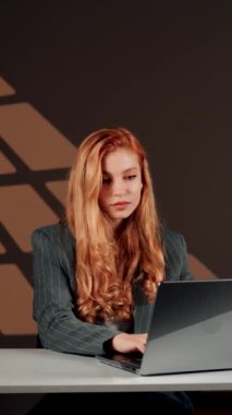 Bir kadın ofisteki başarısına sevinir. Genç bir kadın dizüstü bilgisayarın başında otururken güler ve sevinir. Mutlu bir serbest çalışanın portresi. Çevrimiçi iş kavramı. Dikey video