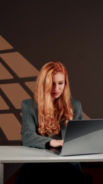 Bir kadın ofisteki başarısına sevinir. Genç bir kadın dizüstü bilgisayarın başında otururken güler ve sevinir. Mutlu bir serbest çalışanın portresi. Çevrimiçi iş kavramı. Dikey video