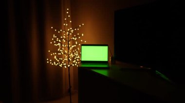 Noel ağacının arka planında yeşil ekranlı bir dizüstü bilgisayar ve çelenkler. Krom anahtar. Noel tatili kavramı