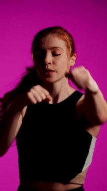 Pembe arka planda dövüş sanatları yapan bir kadın. Dişi bir boksörün portresi. Boks, kickboks, yumruk yumruğa dövüş. Dikey video