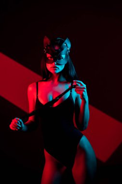 Kedi maskeli bir kadın siyah arka planda kırbaçla poz veriyor. Kamçı bir kadının elindedir. Rol yapma oyunları. BDSM konsepti