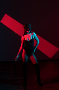 Kedi maskeli bir kadın siyah arka planda kırbaçla poz veriyor. Kamçı bir kadının elindedir. Rol yapma oyunları. BDSM konsepti