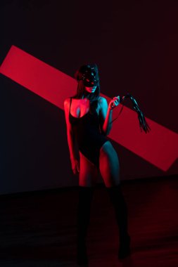 Kedi maskeli bir kadın siyah arka planda kırbaçla poz veriyor. Kamçı bir kadının elindedir. Rol yapma oyunları. BDSM konsepti