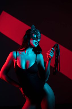 A woman in a cat mask poses with a whip on a black background. The whip is in the hands of a woman. Role-playing games. BDSM concept clipart