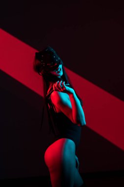 Kedi maskeli bir kadın siyah arka planda kırbaçla poz veriyor. Kamçı bir kadının elindedir. Rol yapma oyunları. BDSM konsepti