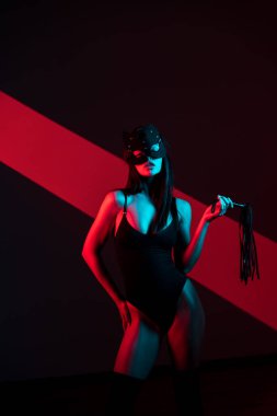 Kedi maskeli bir kadın siyah arka planda kırbaçla poz veriyor. Kamçı bir kadının elindedir. Rol yapma oyunları. BDSM konsepti