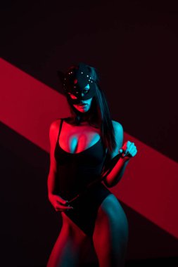 Kedi maskeli bir kadın siyah arka planda kırbaçla poz veriyor. Kamçı bir kadının elindedir. Rol yapma oyunları. BDSM konsepti