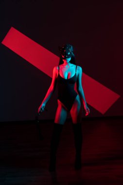 Kedi maskeli bir kadın siyah arka planda kırbaçla poz veriyor. Kamçı bir kadının elindedir. Rol yapma oyunları. BDSM konsepti