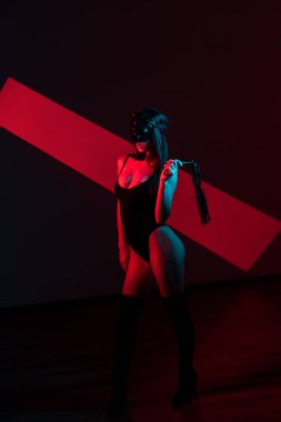 Kedi maskeli bir kadın siyah arka planda kırbaçla poz veriyor. Kamçı bir kadının elindedir. Rol yapma oyunları. BDSM konsepti