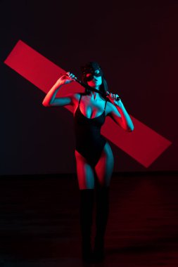 Kedi maskeli bir kadın siyah arka planda kırbaçla poz veriyor. Kamçı bir kadının elindedir. Rol yapma oyunları. BDSM konsepti