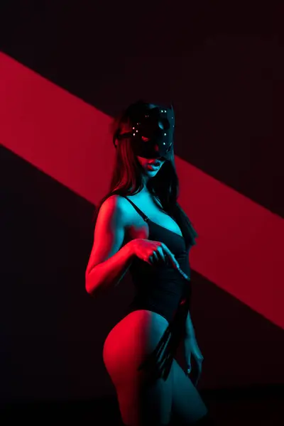 Kedi maskeli bir kadın siyah arka planda kırbaçla poz veriyor. Kamçı bir kadının elindedir. Rol yapma oyunları. BDSM konsepti