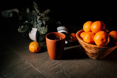 Bir kase mandalinanın yanında, şenlikli mevsim boyunca ahşap masa üzerinde bir bardak sıcak şarap.