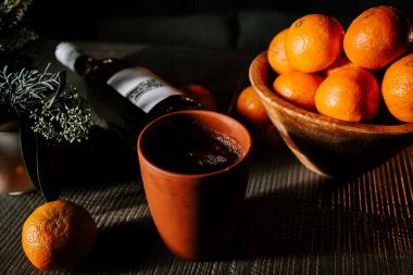 Bir kase mandalinanın yanında, şenlikli mevsim boyunca ahşap masa üzerinde bir bardak sıcak şarap.
