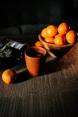 Bir kase mandalinanın yanında, şenlikli mevsim boyunca ahşap masa üzerinde bir bardak sıcak şarap.