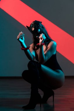 Ellerinde kelepçe olan kedi maskeli bir kadın. Vücut giysili seksi bir kadının portresi. BDSM konsepti. Sevgililer Günü.