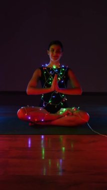 Vücudunda çelenklerle Noel atmosferinde meditasyon yapan bir kadın. Noel yogası. Noel konsepti. Dikey video 4k