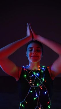 Vücudunda çelenklerle Noel atmosferinde meditasyon yapan bir kadın. Noel yogası. Noel konsepti. Dikey video 4k