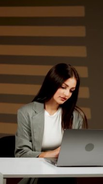 Başarılı bir kadın, modern bir ofiste dizüstü bilgisayarda çalışır, çevrimiçi işleri yönetir ve müşterilerle iletişim kurar. Çevrimiçi iş konseri. Dikey video