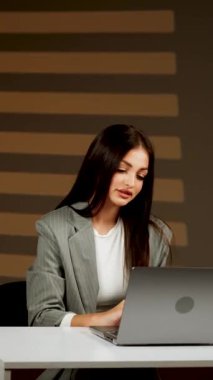 Başarılı bir kadın, modern bir ofiste dizüstü bilgisayarda çalışır, çevrimiçi işleri yönetir ve müşterilerle iletişim kurar. Çevrimiçi iş konseri. Dikey video