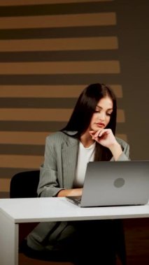 Başarılı bir kadın, modern bir ofiste dizüstü bilgisayarda çalışır, çevrimiçi işleri yönetir ve müşterilerle iletişim kurar. Çevrimiçi iş konseri. Dikey video
