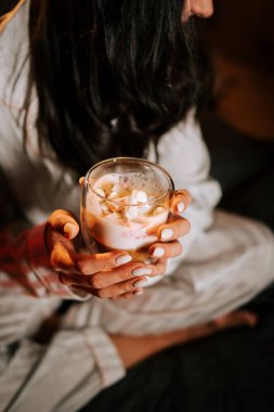 Sıcak kapuçinonun tadını çıkaran bir kadın Marshmallowlu Yatakta dinlenirken Gece Noel süsleriyle çevrili