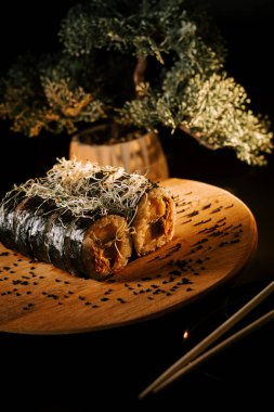 Delicious Sushi Rolls Served on Wooden Plate With Chopsticks in Serene Setting Surrounded by Greenery clipart