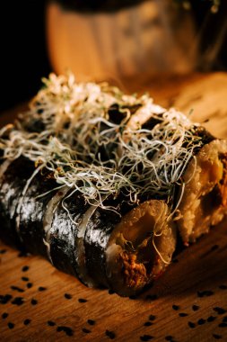 Ahşap tabakta servis edilen lezzetli suşi ruloları Serene ayarlarıyla çevrili yeşil çubuklarla servis ediliyor.