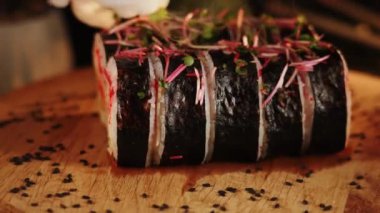 Lezzetli suşi ruloları ahşap bir tahtanın üzerinde döner. Canlı renklerde taze malzemeler sergiler.