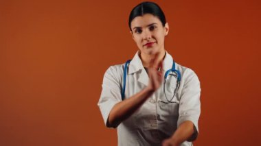Beyaz önlüklü kadın doktor ve turuncu arka planda duran steteskop.