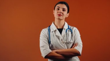 Beyaz önlüklü kadın doktor ve turuncu arka planda duran steteskop.