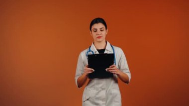 Beyaz önlüklü kadın doktor ve turuncu arka planda duran steteskop.