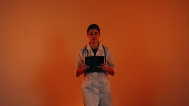 Beyaz önlüklü kadın doktor ve turuncu arka planda duran steteskop.