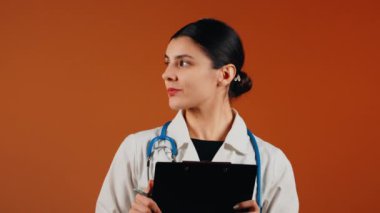 Beyaz önlüklü kadın doktor ve turuncu arka planda duran steteskop.