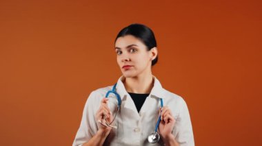 Beyaz önlüklü kadın doktor ve turuncu arka planda duran steteskop.