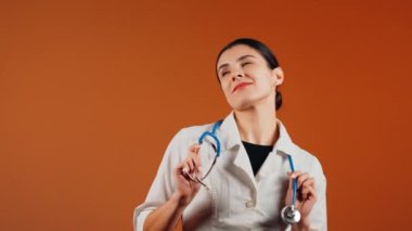 Beyaz önlüklü kadın doktor ve turuncu arka planda duran steteskop.