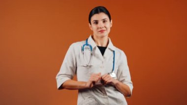 Beyaz önlüklü kadın doktor ve turuncu arka planda duran steteskop.