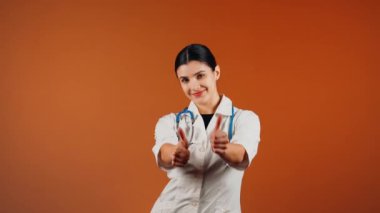 Beyaz önlüklü kadın doktor ve turuncu arka planda duran steteskop.