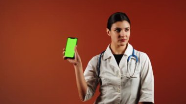 Kadın doktor, canlı bir ortamda yeşil ekranlı, pediatrik ilaç içeren bir telefon tutuyor.