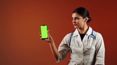 Kadın doktor, canlı bir ortamda yeşil ekranlı, pediatrik ilaç içeren bir telefon tutuyor.