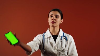 Kadın doktor, canlı bir ortamda yeşil ekranlı, pediatrik ilaç içeren bir telefon tutuyor.