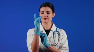 Beyaz önlüklü bir kadın çocuk doktorunun portresi mavi arka planda tıbbi muayeneye hazırlanıyor.