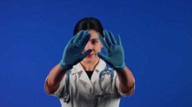 Beyaz önlüklü bir kadın çocuk doktorunun portresi mavi arka planda tıbbi muayeneye hazırlanıyor.