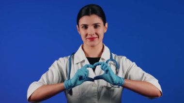 Beyaz önlüklü bir kadın çocuk doktorunun portresi mavi arka planda tıbbi muayeneye hazırlanıyor.