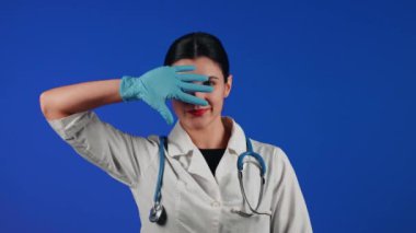 Beyaz önlüklü bir kadın çocuk doktorunun portresi mavi arka planda tıbbi muayeneye hazırlanıyor.