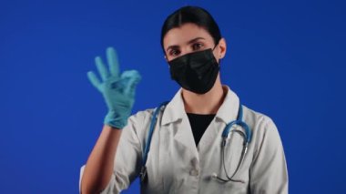 Mavi arka planda siyah bir tıbbi maske takan kadın sağlık çalışanı. Bir doktorun portresi. Viroloji ve salgın konsepti