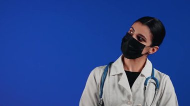 Mavi arka planda siyah bir tıbbi maske takan kadın sağlık çalışanı. Bir doktorun portresi. Viroloji ve salgın konsepti